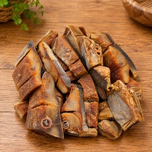 May include: A pile of dried, salted fish chunks with golden-brown skin and translucent, firm flesh. The pieces are irregularly cut, showing visible bone structures and a textured, cured surface. The fish segments are stacked together in a cluster.