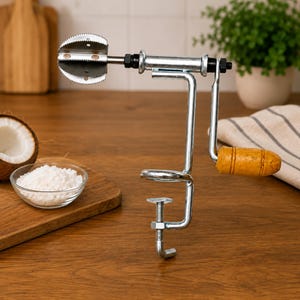 May include: A silver metal coconut grater tool featuring a serrated circular blade, a hand-crank mechanism with a wooden handle, and a screw-style clamp base for securing the device to a flat surface during operation for manual food preparation.