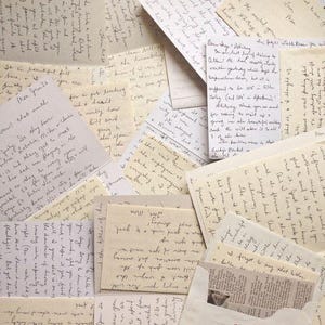 May include: A collection of overlapping handwritten letters and notes on cream and white paper. The documents feature cursive and print handwriting in black and blue ink, with various dates and personal messages visible across the scattered pages.