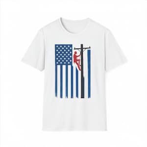 Puede incluir: Una camiseta blanca de manga corta con un estampado gráfico en el pecho. El diseño muestra una bandera estadounidense estilizada en azul y blanco, con la silueta roja de un trabajador subiendo a un poste eléctrico negro en el centro.
