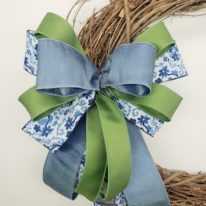 May include: A wreath with a blue and green bow. The bow is made of three different ribbons: a blue satin ribbon, a green satin ribbon, and a blue and white patterned ribbon.