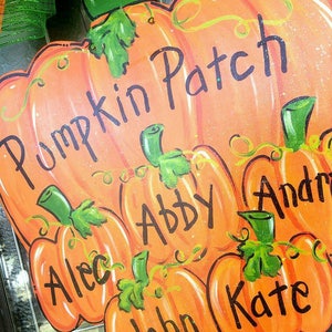 May include: A wooden pumpkin-shaped sign with the words "Pumpkin Patch" and the names Alec, Abby, John, Andrew, and Kate. The sign is painted orange with green accents and black lettering, perfect for fall decor.