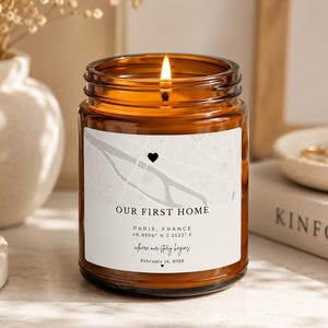 Peut inclure: Une bougie allumée dans un pot en verre ambré avec une étiquette blanche présentant un graphique de carte, un petit cœur noir et le texte : OUR FIRST HOME, PARIS, FRANCE, 48.8566 N 2.3522 E, where our story begins, et February 14, 2023.