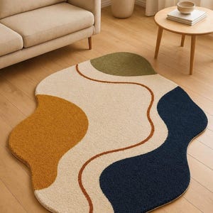 May include: An area rug with an irregular, organic shape featuring a cream-colored base with abstract color-blocked sections in mustard yellow, olive green, and navy blue, separated by thin, curved, rust-colored lines on a textured surface.