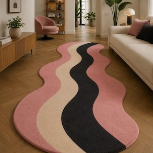 May include: An elongated, wavy-shaped area rug featuring a repeating pattern of thick, curved stripes in dusty pink, cream, and charcoal black. The rug has a soft, textured pile and follows a fluid, organic silhouette that stretches across the floor.