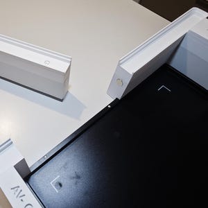 Puede incluir: Un conjunto de marco modular blanco con una placa base rectangular negra que presenta el texto XTOOL. El sistema incluye un componente lateral rectangular blanco separado y una varilla cil&iacute;ndrica blanca unida a la estructura.