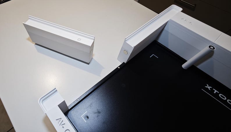 Puede incluir: Un conjunto de marco modular blanco con una placa base rectangular negra que presenta el texto XTOOL. El sistema incluye un componente lateral rectangular blanco separado y una varilla cil&iacute;ndrica blanca unida a la estructura.