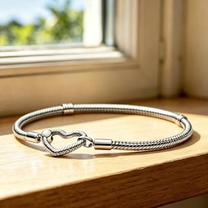 May include: A silver-toned snake chain bracelet featuring a heart-shaped clasp. The bracelet has a textured, flexible design with smooth metal end caps that connect to the central heart closure, creating a continuous circular loop of polished metal.