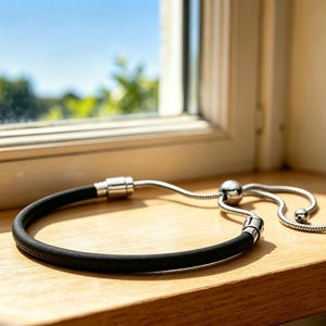 May include: A black cord bracelet featuring a silver-toned metal sliding clasp mechanism. The design includes a flexible snake chain extension with two small silver-toned metal beads at the ends, allowing for an adjustable fit around the wrist.