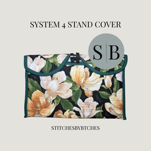 May include: A quilted System 4 stand cover featuring a floral pattern of white and yellow magnolia blossoms with green leaves on a black background. The cover has a dark green trim and a central black clasp. Text reads SYSTEM 4 STAND COVER and STITCHESBYBTCHES.