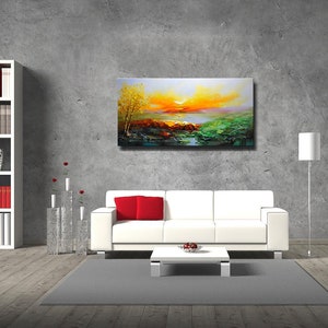 K&ouml;nnte beinhalten: Ein wei&szlig;es Sofa mit roten Kissen steht vor einer grauen Wand mit einem Landschaftsbild dar&uuml;ber. Das Bild zeigt einen Sonnenuntergang &uuml;ber einem See mit B&auml;umen und Felsen im Vordergrund.