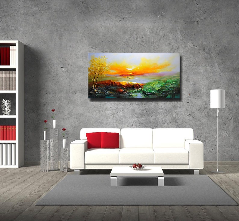 K&ouml;nnte beinhalten: Ein wei&szlig;es Sofa mit roten Kissen steht vor einer grauen Wand mit einem Landschaftsbild dar&uuml;ber. Das Bild zeigt einen Sonnenuntergang &uuml;ber einem See mit B&auml;umen und Felsen im Vordergrund.