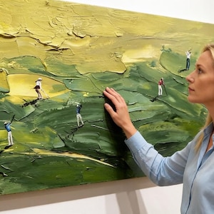 Op de afbeelding: Een olieverfschilderij dat een golfbaan afbeeldt met miniatuurfiguren die golf spelen. Het kunstwerk heeft getextureerde penseelstreken in groen- en geeltinten. Een vrouw in een blauw overhemd raakt het schilderij aan.