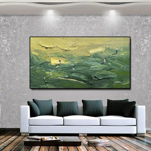 Op de afbeelding: Een olieverfschilderij dat een golfbaan met verschillende golfers afbeeldt. Het kunstwerk heeft een textuur, impasto-stijl met groen- en geeltinten. Het schilderij is zwart omlijst en hangt boven een witte bank met donkergroene kussens.