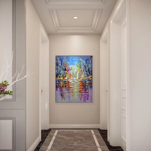 Puede incluir: Una pintura abstracta colorida de un horizonte urbano reflejado en el agua. La pintura est&aacute; en un pasillo con paredes blancas y un techo blanco.