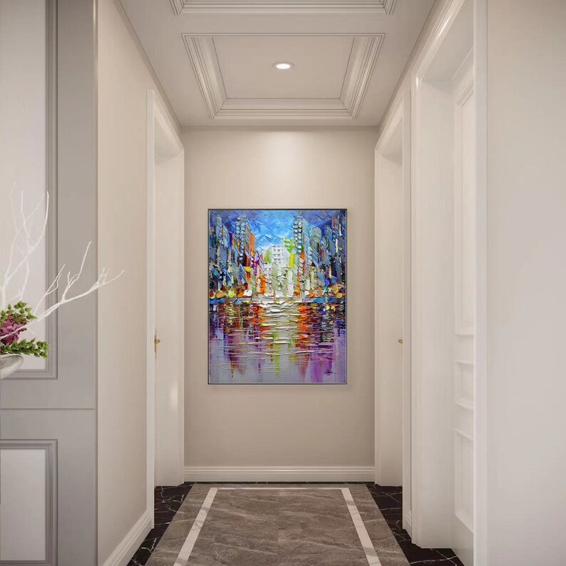 Puede incluir: Una pintura abstracta colorida de un horizonte urbano reflejado en el agua. La pintura est&aacute; en un pasillo con paredes blancas y un techo blanco.