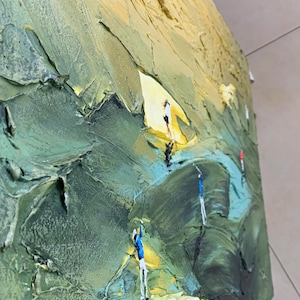 Op de afbeelding: Getextureerd olieverfschilderij dat een landschap met figuren uitbeeldt. Het kunstwerk gebruikt een palet van groen en geel, met zichtbare penseelstreken die een driedimensionaal effect cre&euml;ren. Kleine figuren in wit, blauw en rood zijn verspreid.