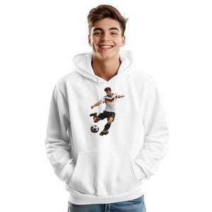 May include: A white hooded sweatshirt featuring a graphic print of a soccer player in a black, red, and gold jersey kicking a soccer ball. The hoodie includes a front kangaroo pocket, long sleeves, and a drawstring hood, providing a clean look.