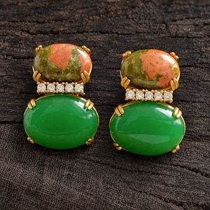 May include: A pair of gold-tone earrings featuring an oval-shaped mottled green and pink stone at the top, a row of five small clear round stones in the center, and a smooth, solid oval-shaped bright green stone at the bottom.