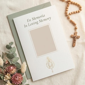 May include: A white memorial card featuring the text En Memoria In Loving Memory, a central rectangular frame for a photo, and a gold illustration of the Virgin of Guadalupe. A wooden rosary with a crucifix and dried flowers are placed nearby.
