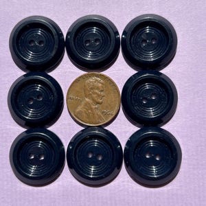 May include: Nine navy blue buttons with two holes each, arranged in a grid. A copper penny from 1964 is centered among the buttons. The buttons have a ridged design around the edges.