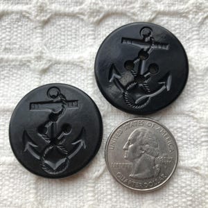 May include: Two black plastic buttons with an anchor design. The buttons have three holes for sewing.