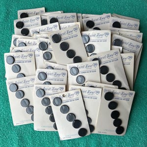 May include: A collection of vintage Jewel-Tone brand buttons mounted on individual cream-colored cardboard cards. Each card features black text reading Jewel-Tone, 29 cents, and to launder and dry clean. The buttons are round, black, and glossy.