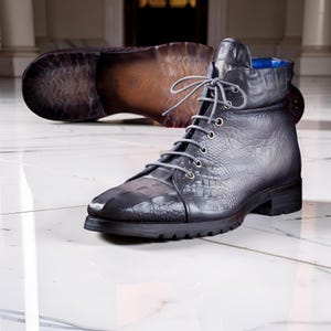 May include: A dark grey lace-up ankle boot featuring a textured crocodile-embossed leather upper, silver-toned metal eyelets, grey laces, and a black lug sole. The interior lining is a vibrant blue, and the boot is shown with its sole visible.