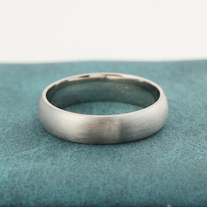 Peut inclure: Une bague en métal argenté avec une finition brossée et mate, présentant un profil arrondi et bombé. L'anneau affiche une texture lisse et uniforme sur toute sa surface extérieure, révélant un design circulaire simple et creux.