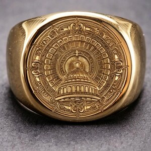 May include: A gold-toned signet ring featuring a detailed circular engraving of a domed building, reminiscent of the United States Capitol, centred within a radiating sunburst pattern and ornate decorative filigree borders on the face.