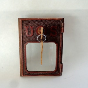 May include: A vintage brass mailbox with a glass window and a key in the lock. The mailbox has the letters "U.S." embossed on the front.