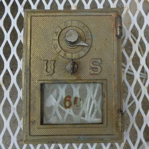 May include: A vintage brass mailbox with the letters "U S" and the number "60" visible. The mailbox has a dial with numbers and a small keyhole. The mailbox is set against a white diamond-patterned background.