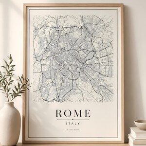 Puede incluir: Una lámina enmarcada con un mapa de Roma, Italia, que muestra una cuadrícula de calles detallada en blanco y negro sobre un fondo crema. El texto ROME, ITALY y La Città Eterna aparece impreso en negro en la parte inferior, con marco de madera.