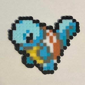 May include: A pixel art figure crafted from fused plastic beads, depicting a stylized creature with a rounded head and a tail. The design features a color palette of light blue, dark blue, yellow, white, orange, and grey, outlined in black.