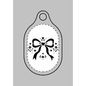 May include: A black and white tag with a bow and floral design. The tag has a white oval center with a black bow, hearts, and floral accents. The tag has a hole at the top for hanging.