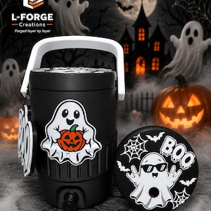 May include: A black beverage cooler with a white handle and a spigot, featuring a white ghost holding an orange pumpkin. A matching circular lid displays a ghost wearing sunglasses, spiderwebs, bats, and the text BOO. A ghost-shaped tag hangs nearby.