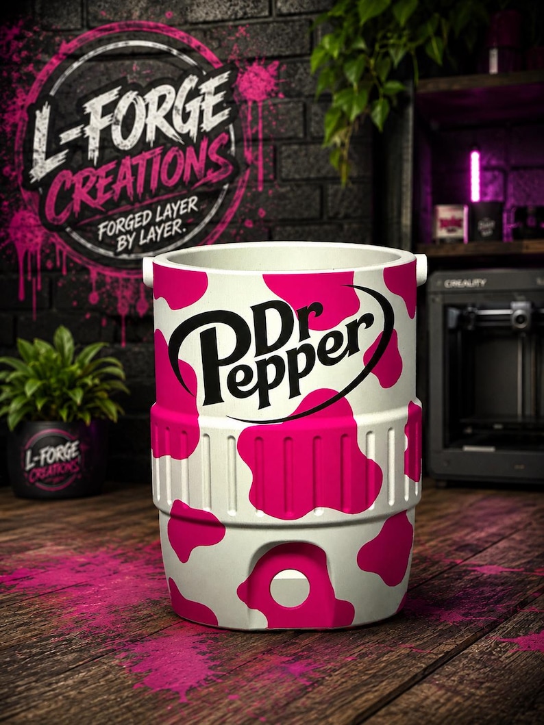 Pu&ograve; includere: Un refrigeratore cilindrico bianco caratterizzato da un vivace motivo a macchie di mucca rosa e dal logo nero Dr Pepper stampato sul davanti. Il refrigeratore presenta una fascia centrale testurizzata e un pulsante bianco circolare.