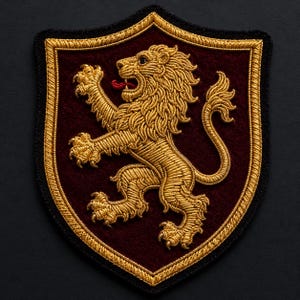 May include: A shield-shaped embroidered patch featuring a gold lion rampant on a deep burgundy felt background. The lion is depicted in profile with a red tongue, surrounded by a thick gold braided border and a thin black outer edge trim.