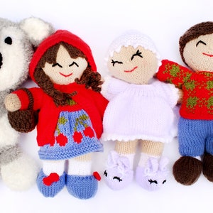 Puede incluir: Cuatro juguetes de peluche de punto: un oso gris, una niña con un vestido rojo con capucha, una niña con un vestido blanco y un niño con un suéter rojo y verde y pantalones azules.