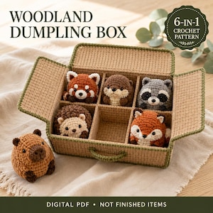 Może przedstawiać: Wzór szydełkowy zatytułowany WOODLAND DUMPLING BOX 6-IN-1 CROCHET PATTERN przedstawiający prostokątne pudełko w kolorze opalenizny z zielonym wykończeniem, zawierające pięć małych szydełkowanych zwierząt leśnych: pandę rudą, wydrę, szopa, jeża, lisa i kapibarę.