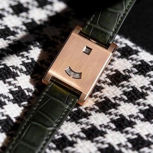 May include: A rectangular rose gold wristwatch with a brushed metal finish, featuring a dark green alligator-textured leather strap. The watch face displays the number 10 in a small square window and a curved gauge showing the numbers 0, 55, and 60.