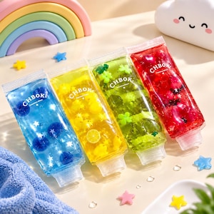 Puede incluir: Cuatro tubos de plástico transparente rellenos de slime de colores azul, amarillo, verde y rojo. Cada tubo tiene la etiqueta CHBOK Premium Slime y contiene pequeñas formas decorativas como estrellas, rodajas de cítricos y tréboles.