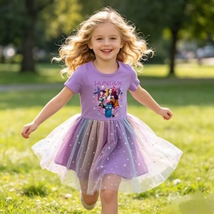 May include: A short-sleeved lavender dress featuring a graphic print with the text HUNTRAX and stylized characters. The skirt is made of layered, multicolored tulle fabric adorned with small white star patterns over a solid lavender base.