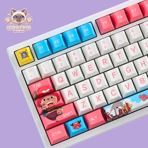 May include: A mechanical keyboard featuring white keycaps with pink lettering, blue function keys, and pink keys. The tab key displays a cartoon character in a red hat, while the spacebar features a ship illustration and the text "Chopper".