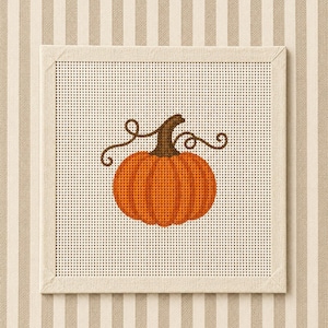 May include: A square needlepoint canvas featuring a centred orange pumpkin with a brown stem and two dark brown curly vines. The design is stitched onto a white grid fabric, which is mounted within a light beige fabric-covered square frame.