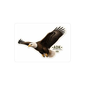 May include: A die-cut sticker featuring a bald eagle in flight with brown feathers, a white head, and a yellow beak. To the right of the eagle, the text ADK is printed above the words BURTON NORTH DESIGNS, accompanied by small pine tree icons.