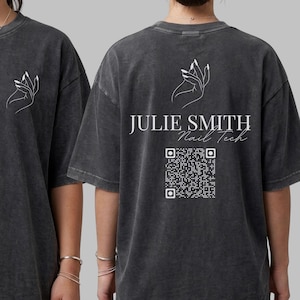 May include: A charcoal gray mineral-washed t-shirt featuring a white line-art hand graphic on the front and back. The back displays the text JULIE SMITH Nail Tech above a white QR code. The design is printed in white ink on the dark fabric.