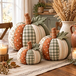 May include: Three fabric pumpkins in varying sizes, featuring patchwork panels of orange floral print, green gingham, and cream-coloured stripes. Each pumpkin is topped with a fabric stem and a single green quilted leaf accent.
