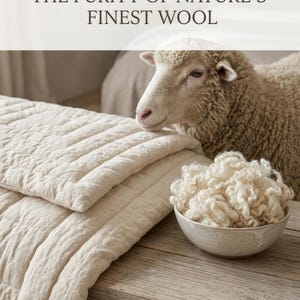 Könnte beinhalten: Eine cremefarbene, gesteppte Wolldecke, eine Schale mit rohen weißen Wollfasern und ein Schaf. Der Text THE PURITY OF NATURE'S FINEST WOOL ist oben zu sehen. Die Gegenstände sind auf einer Holzoberfläche angeordnet.