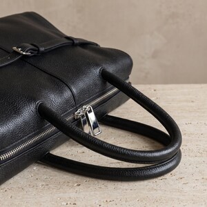 Detail of the twin rolled top handles and secure top zipper closure on the textured black leather office handbag, showcasing polished silver-tone hardware and clean stitching.